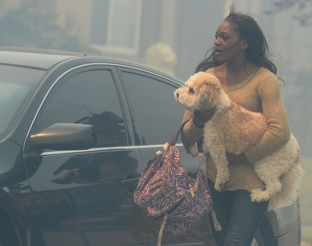 A woman evacuating her home carries a dog to a vehicle in smoke from the Etiwanda Fire in Rancho Cucamonga, Calif., on Wednesday. The wildfire driven by surging Santa Ana winds sent a choking pall of smoke through foothill neighborhoods. No homes burned, but the smoke prompted mandatory evacuation orders for several areas of town.