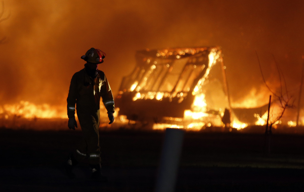 A firefighter walks past a burning mobile home at a mobile home park near Prairie Grove Rd. and Douglas during Oklahoma wildfires in south Logan County, Sunday, May 4, 2014. Firefighters worked through the night and into early Monday to battle a large wildfire that destroyed at least six homes and left at least one person dead after a controlled burn spread out of control in central Oklahoma.