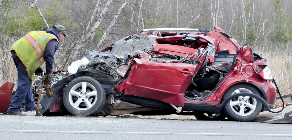 The crumpled wreckage of a small car is examined after a collision with a Vassalboro school bus that was parked on Route 3 in South China on Monday.