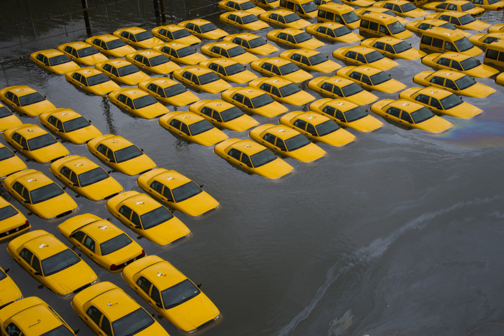 In this Oct. 30, 2012 file photo, a parking lot full of yellow cabs in Hoboken, N.J. is flooded as a result of Superstorm Sandy. Global warming is rapidly turning America the beautiful into America the stormy, sneezy and dangerous, according to the National Climate Assessment report released Tuesday, May 6, 2014.