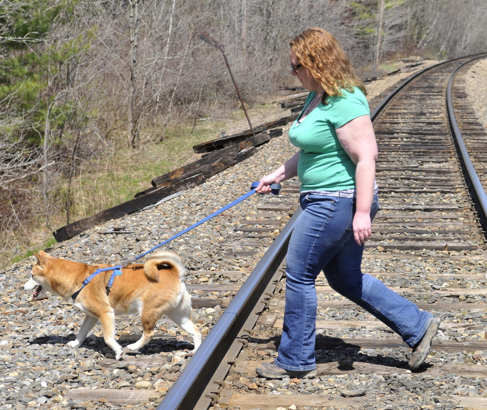 Miriam Easton and her dog cross one of the two train tracks that bisect her family’s 80 acres in Oakland on Thursday. A long train on the tracks blocks a trail that the Easton family has maintained for generations.