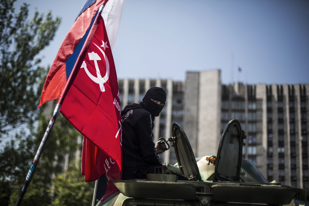 A masked pro Russia man is seen atop an APC flying a Russian flag, top, and a Donetsk People’s Republic flag, as it stands in front of the occupied administration building in Donetsk, Ukraine, on Saturday.