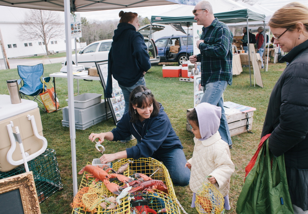 Sue Nelson of Potts Harbor Lobster in Harpswell shows Maple Gauthier, 3, of Brunswick how to tend to a lobster trap during the Crystal Springs Farmers Market in Brunswick on May 3.