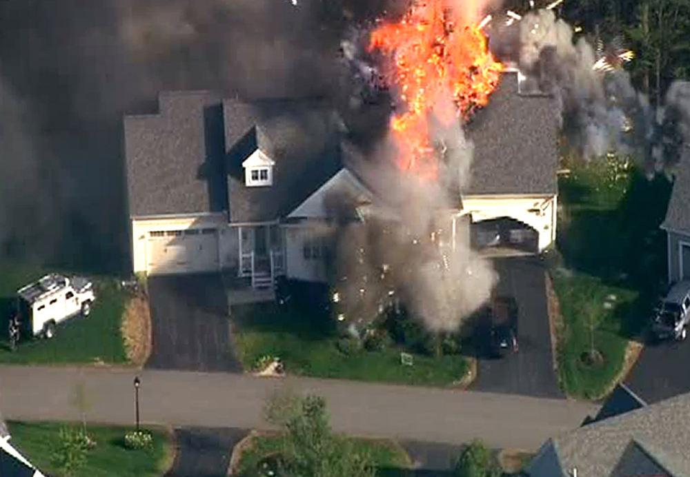In these frame grabs from television helicopter video, a police SWAT team, left, is parked on the lawn of a home in Brentwood, N.H., as it explodes into flames, Monday, May 12, 2014. Shots were fired just before the fire, which involved a police officer, according to the New Hampshire State Police.