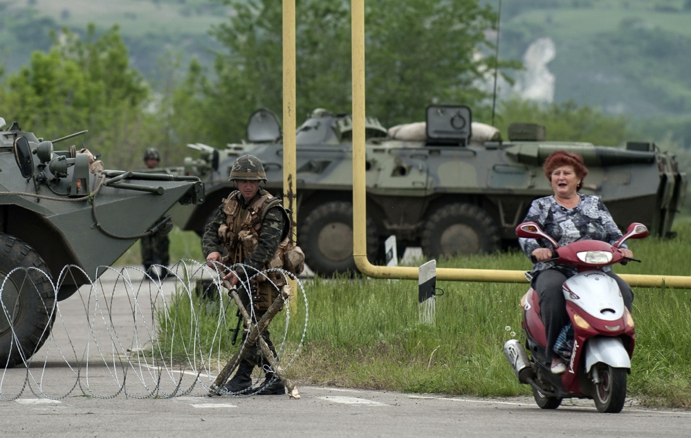 A woman rides a scooter passing a Ukrainian army checkpoint on the main road to Spivakovka village in the eastern Ukraine, 60km (36 miles) outside in Luhansk, Ukraine, Monday, May 12, 2014. Pro-Moscow insurgents in eastern Ukraine declared independence Monday and sought to join Russia, undermining upcoming presidential elections, strengthening the Kremlin's hand and putting pressure on Kiev to hold talks with the separatists following a referendum on self-rule. (AP Photo/Evgeniy Maloletka)