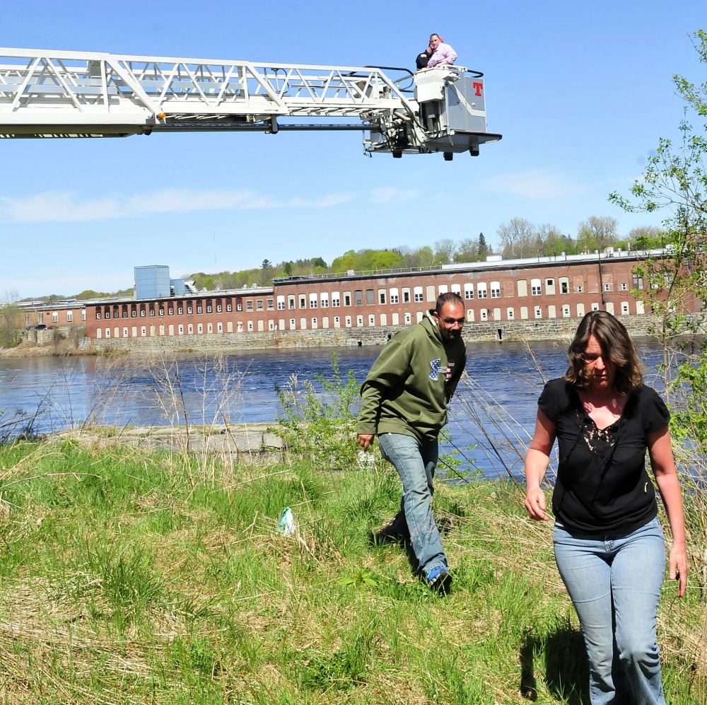 Joe Bradley and Darlene Champagne move as Waterville firefighter Mark Hamilton brings Mary Temple back to the ground in a department ladder truck bucket Tuesday after rescuing her from a granite abutment beside the Kennebec River at Head of Falls in Waterville. Temple said she feared climbing down the steep structure.