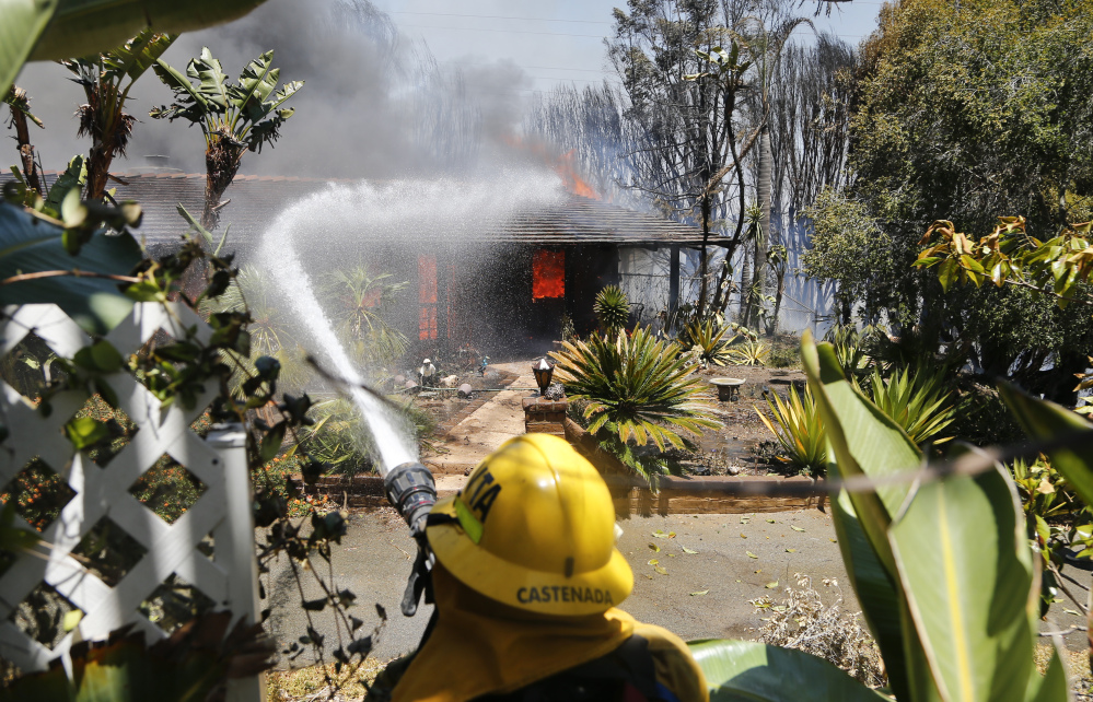 A firefighter pours water on a fully engulfed home Wednesday in Carlsbad, Calif.