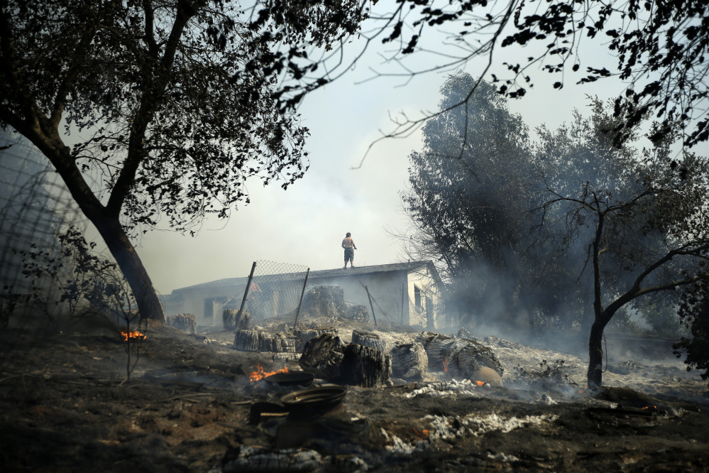 Jeff Brown waters the roof of his home as vegetation smolders during a wildfire Thursday in Escondido, Calif.