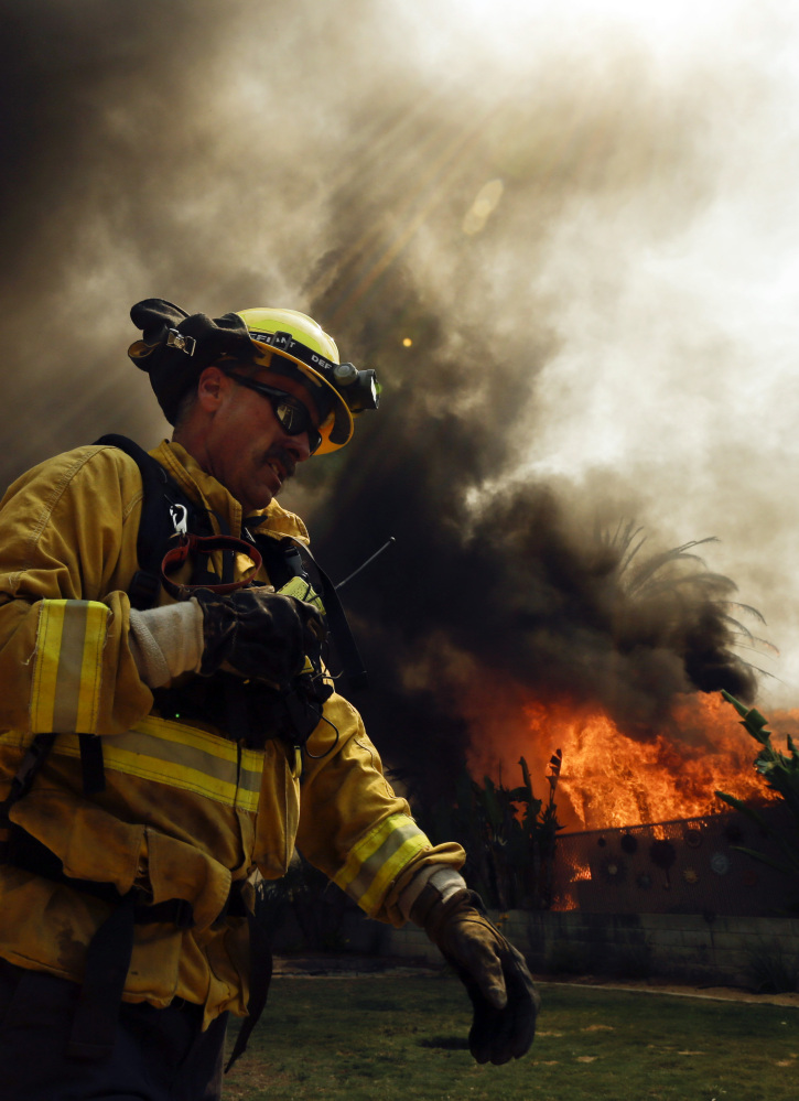 A firefighter moves past a burning structure during a wildfire Thursday in Escondido, Calif.