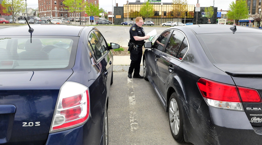 Waterville police Officer Robert Bouley places a map with new parking regulations in The Concourse and a warning that the car was parked longer than the two-hour maximum in Waterville on Thursday.