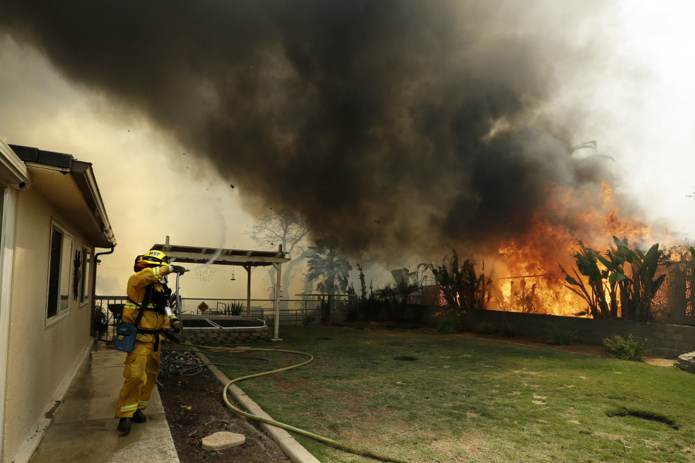 A firefighter moves away as shifting winds bring a plume of smoke from a wildfire Thursday in Escondido, Calif.