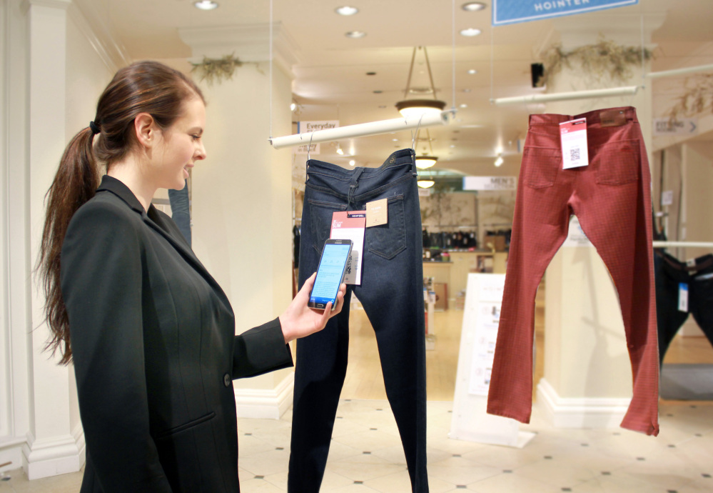 In this photo provided by Hointer, a woman demonstrates the Seattle store’s shopping technology. Hointer displays clothing not in piles or on racks but as one piece hanging at a time, like a gallery. Shoppers touch their smartphones to a coded tag on the item and select a color and size. Technology in the store keeps track of the items, and by the time a shopper is ready to try them on, theyíre already at the dressing room.