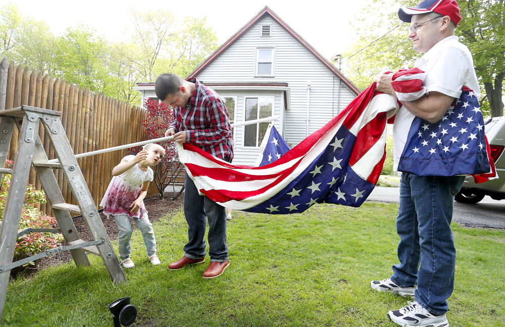 Gary Aldrich, right, his son Phil and granddaughter Jaelynn, 6, hang an American flag at Aldrich’s home in Sanford on Monday. The flag draped the casket during the funeral of Aldrich’s grandfather, a World War I veteran, in 1966 in Old Town.