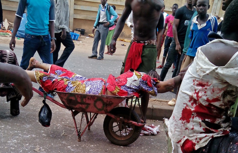An injured woman is carried after bombs exploded at a bus terminal and market in Jos, Nigeria.