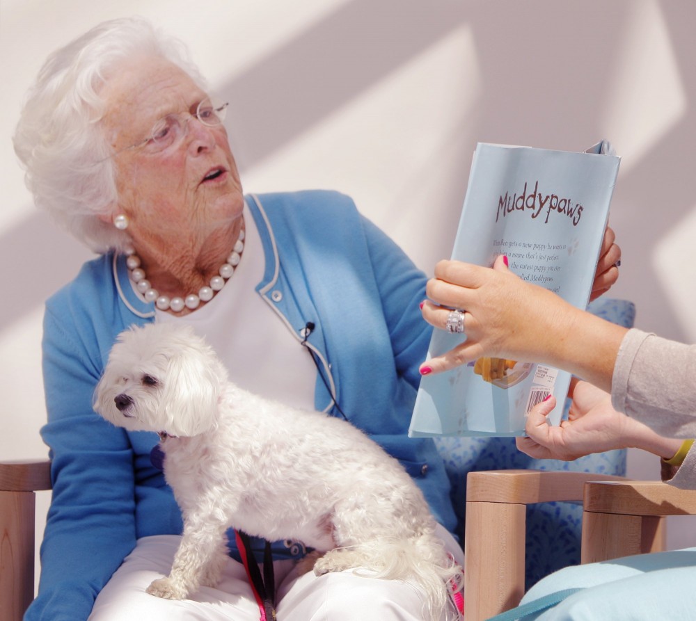 In this July 2012 photo, Barbara Bush reads the book "Muddypaws" to children at the Barbara Bush Children's Hospital at Maine Medical Center in Portland. In her lap is her dog Mini-Me.