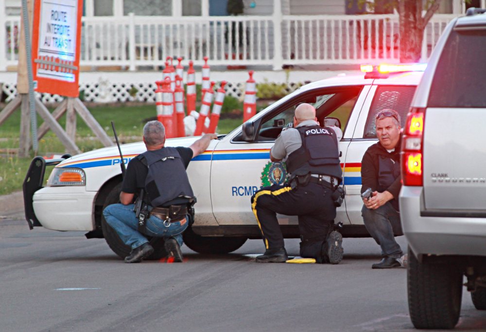 Police officers take cover behind their vehicles at the scene of shootings Wednesday in Moncton, New Brunswick. The Associated Press / Moncton Times & Transcript, Ron Ward via The Canadian Press 