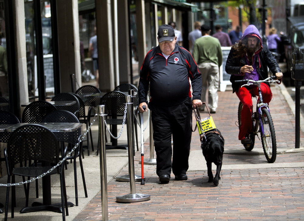 Bud Buzzell, who is visually impaired, walks with his guide dog outside Congress Bar & Grill, which has outdoor seating that appears to leave 4 feet of sidewalk space as required. Gabe Souza/Staff Photographer