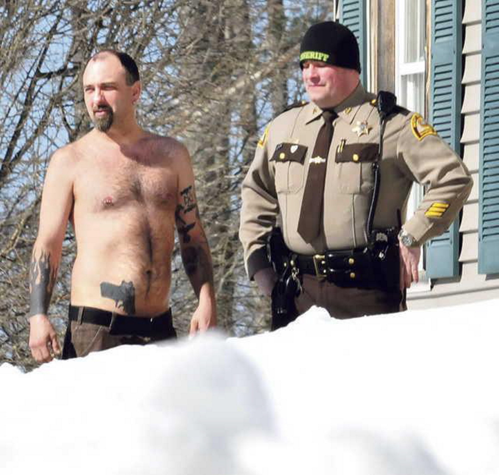 Norridgewock resident Michael Smith stands beside a Somerset County sheriff’s deputy on March 18, after the tattoo of a pistol on his stomach was mistaken for a real firearm.