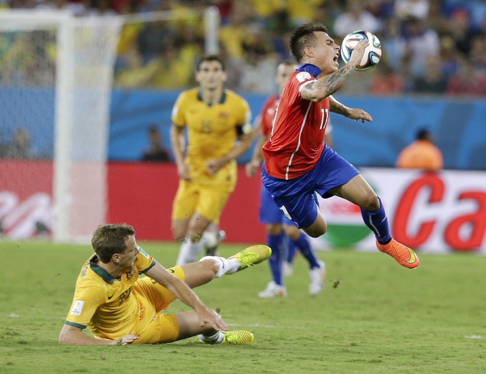 Australia’s Alex Wilkinson, left, trips up Chile’s Eduardo Vargas (11) during the first half of the group B World Cup soccer match between Chile and Australia in the Arena Pantanal in Cuiaba, Brazil, Friday, June 13, 2014.