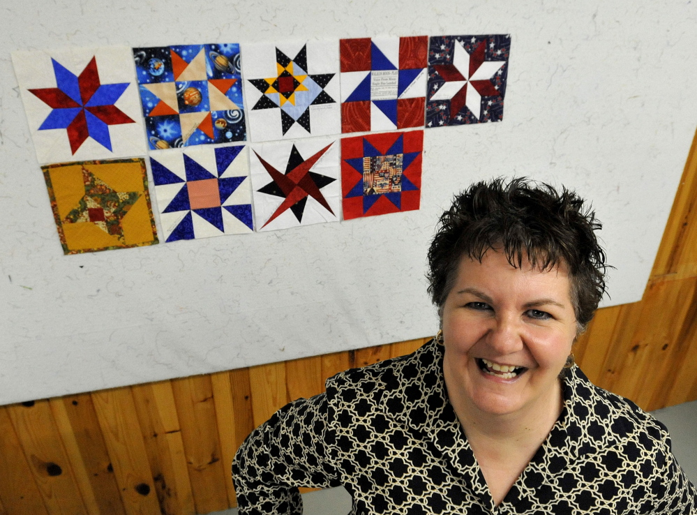 Nadine Villani, a member of the Somerset Samplers, stands next to several quilted squares with space themes at Pinwheels Quilting on West Front Street in Skowhegan.