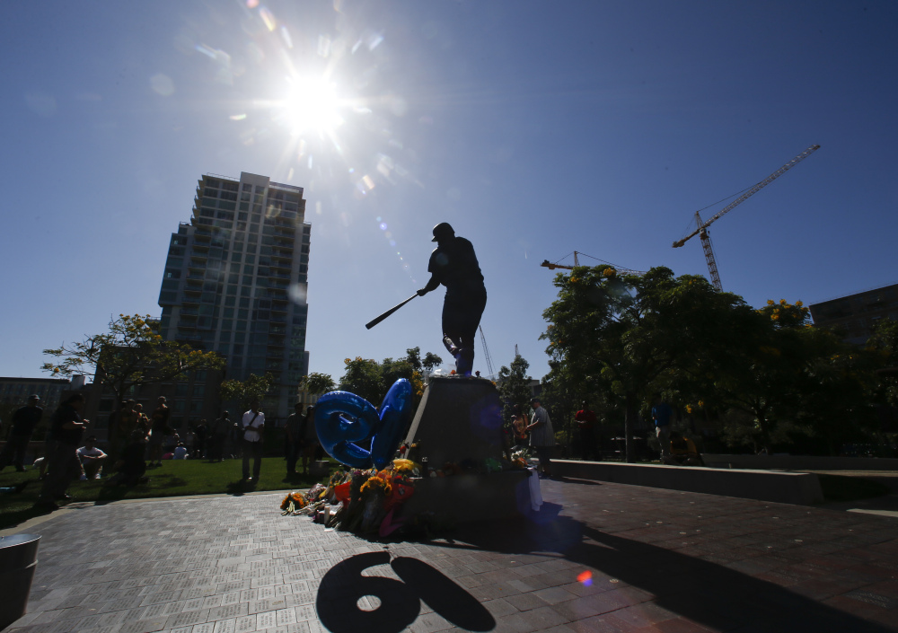 The Tony Gwynn statue "Mr.Padre" is silhouetted against the late afternoon sun as his number "19"  shines through balloons Monday, June 16, 2014, in San Diego. Gwynn, who won eight National League batting titles and was a member of the Baseball Hall of Fame, died Monday at 54 from cancer.  (AP Photo/Lenny Ignelzi)