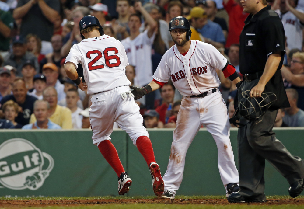 Boston Red Sox’s Brock Holt (26) is congratulated by teammate Dustin Pedroia as he scores on a sacrifice fly by Xander Bogaerts in the third inning.