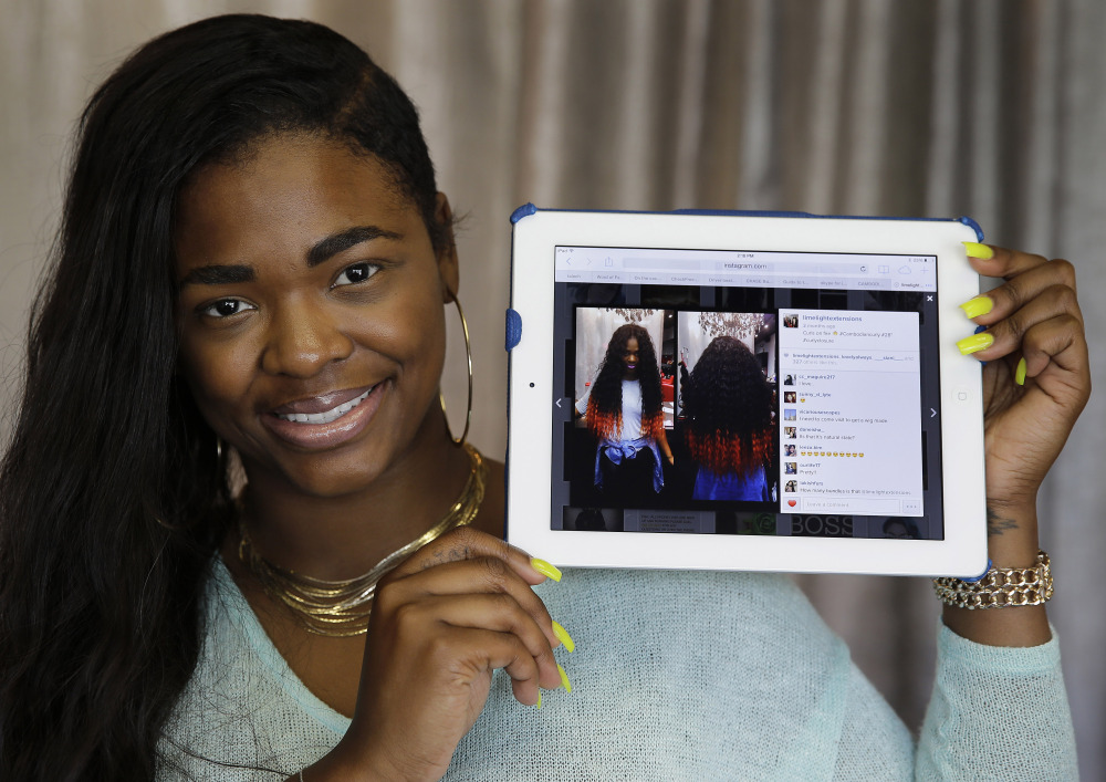Miranda Jade Plater, owner of Limelight Extensions, poses with a tablet showing an Instagram photo of her wearing long, black curly hair extensions with the ends dyed bright orange at her salon in Farmington Hills, Mich., on Wednesday. That photo alone has generated about $10,000 in sales.