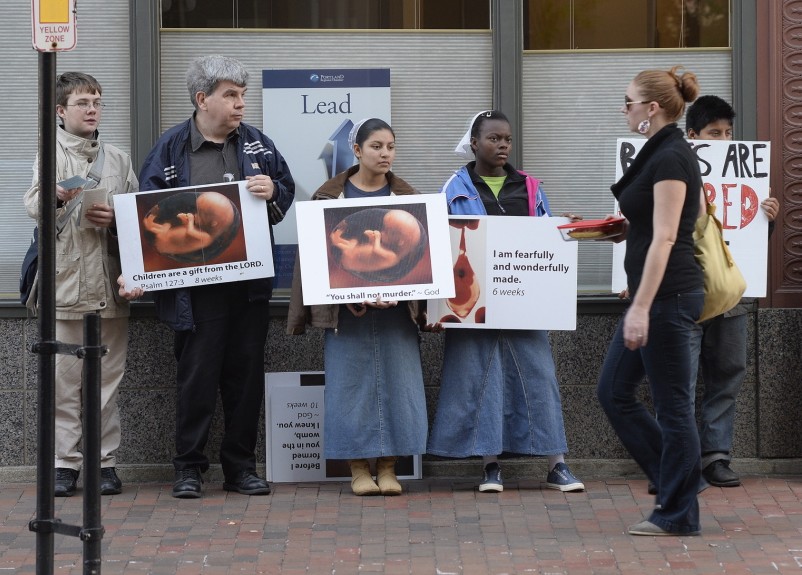 A pedestrian walks past anti-abortion protesters on Congress Street in Portland near the Planned Parenthood clinic in this Oct. 4, 2013, photo.