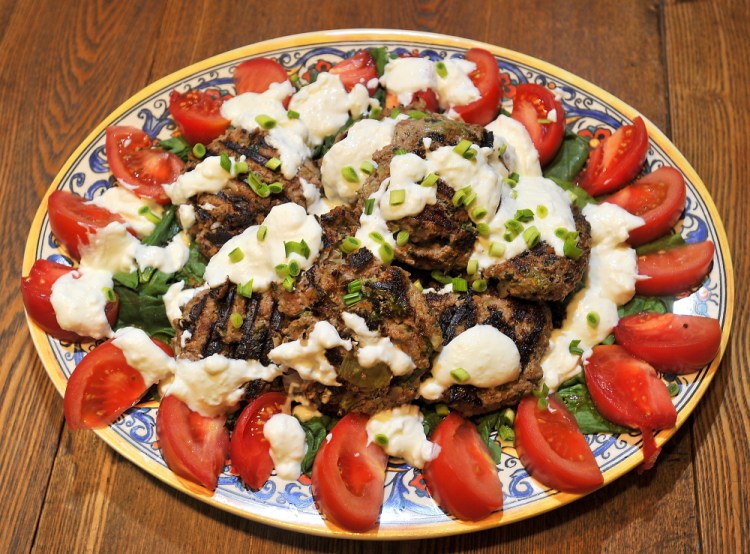 The finished dish: grilled burgers with ground lamb and ground goat meat, fresh mint and grated onion on a bed of sliced tomatoes and wilted spinach and garnished with chopped green garlic. The white sauce is made from sheep milk yogurt mixed with goat milk feta cheese. Gordon Chibroski/Staff Photographer