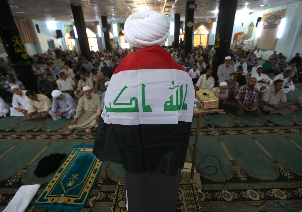 A Shiite cleric, his back covered by an Iraqi flag, prays Friday at a Shiite mosque in the northern oil-rich province of Kirkuk, Iraq.