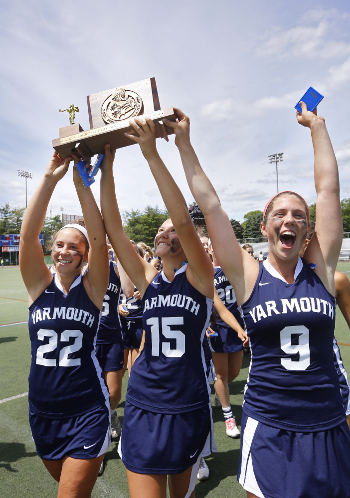Yarmouth captains Julia Primeau, left, Grace O’Donnell and Abby Belisle Haley, right, hold up the state championship trophy after defeating Cape Elizabeth in the Class B title game on Saturday in Portland.