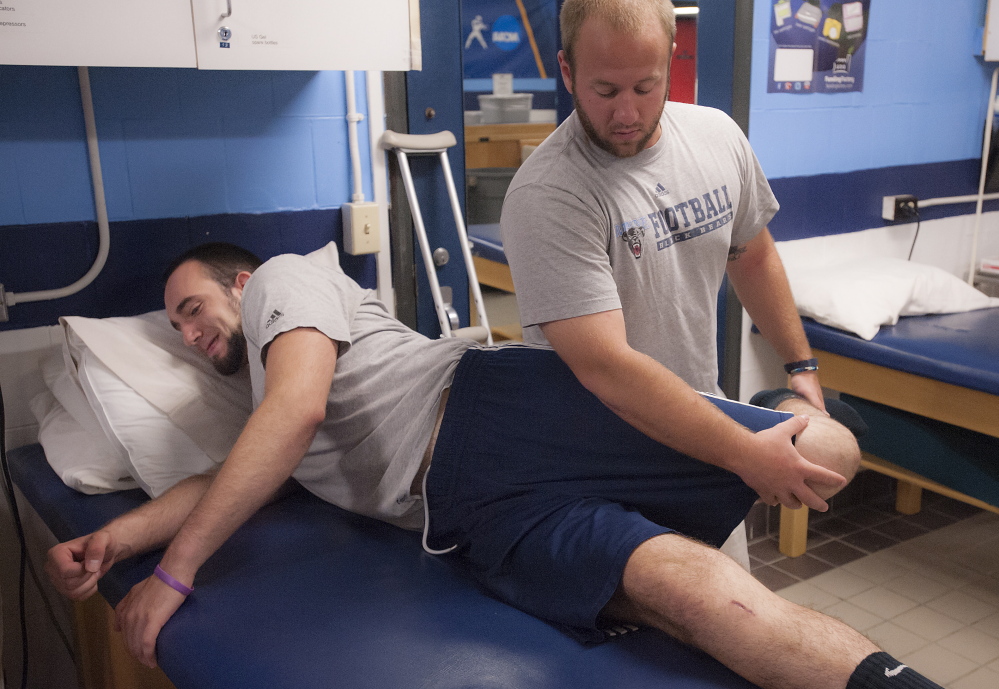 University of Maine trainer Ben Randall works on the left knee of Kurt Massey, a defensive end who tore his ACL during spring practice. “It’s been kind of bad,” Massey said of the loss of summer income and the medical bills his family’s insurance carrier faces.