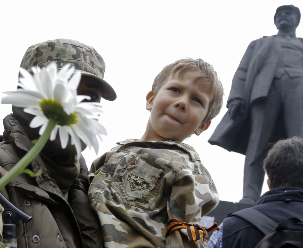 A pro-Russia fighter holds a boy on his hands after taking an oath in eastern Ukraine on Saturday with a statue of Soviet Union founder Vladimir Lenin on the right.
