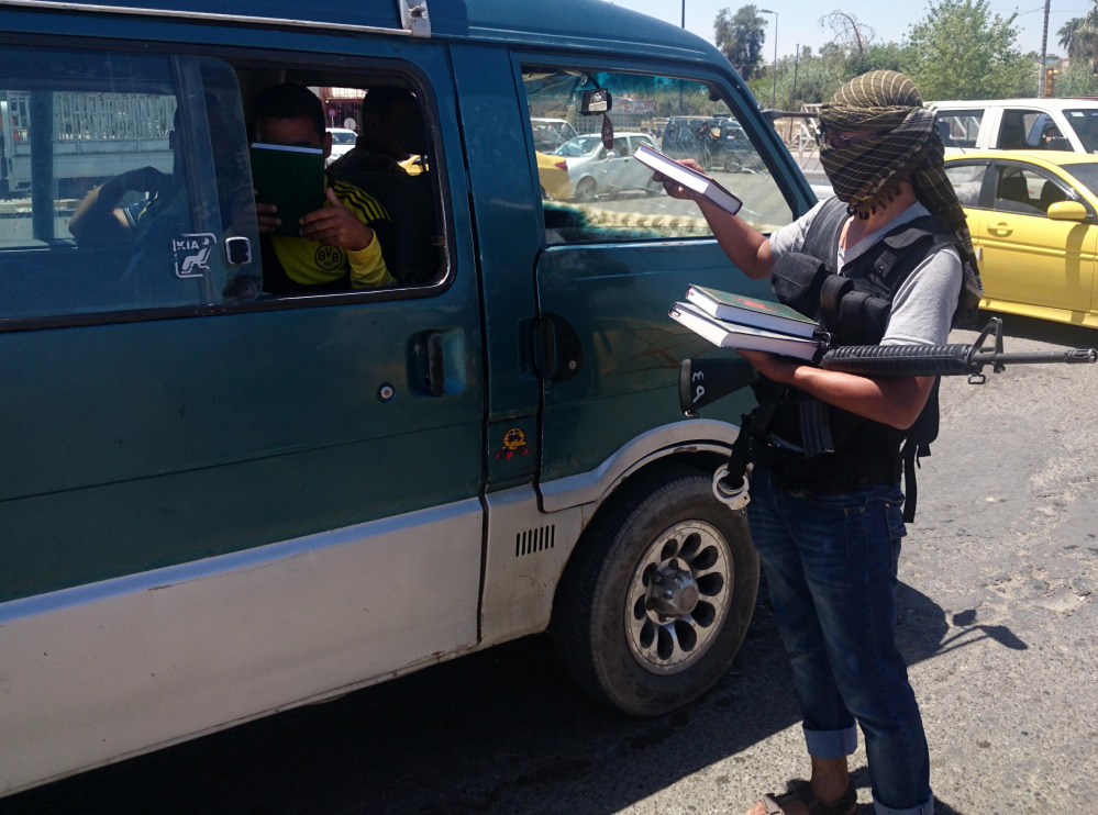 A fighter with the al-Qaida-inspired Islamic State of Iraq and the Levant (ISIL) distributes a copy of the Quran, Islam’s holy book, to a driver in central northern city of Mosul, 225 miles northwest of Baghdad.