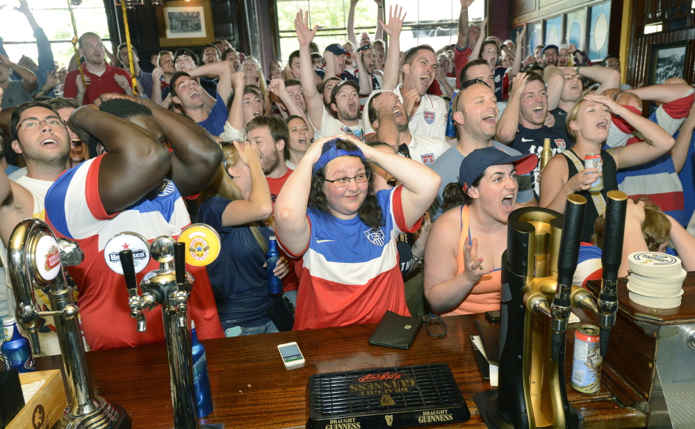Richard Agbortoko of Cameroon, his arms covering his face, reacts to a missed goal with Jessica Donovan, center, of Portland, and Jenna Fabiano of South Portland and the rest of the crowd at RiRa’s in Portland  during the World Cup match that pitted the United States and Germany in Brazil on Thursday.