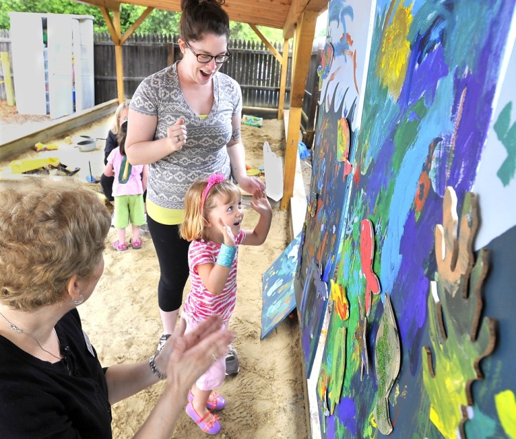 Evelyn Kirby, 3, expresses her joy Thursday after successfully putting fish-shaped cutouts onto a painting of the ocean at Children’s Odyssey, an art-language camp in Portland for pre-schoolers. Speech-language pathologist Laurie Mack, left, from Northeast Hearing and Speech Center and Jacklyn Peters, a fourth-year art education student at the University of Southern Maine, share in Evelyn’s excitement.