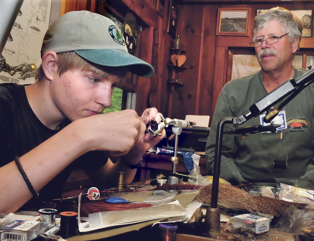 Teenager Sam Kenney concentrates as he learns how to tie a fly under the tutelage of Jim Dunbar of Winslow at the trout camp in Solon on Thursday.