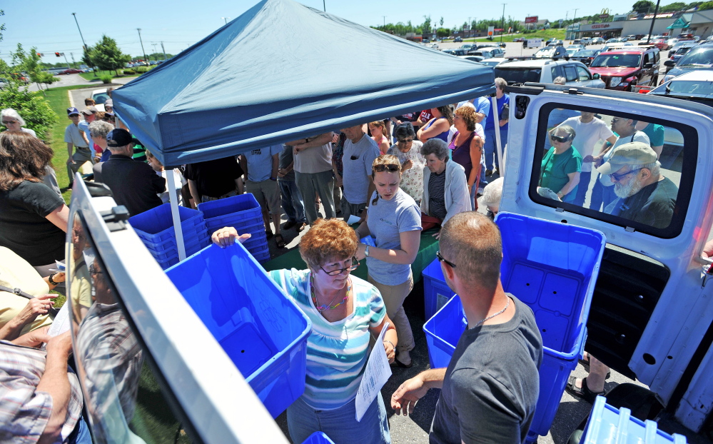 Ecomaine workers distribute free recycling bins to the public at Elm Plaza in Waterville on Friday.