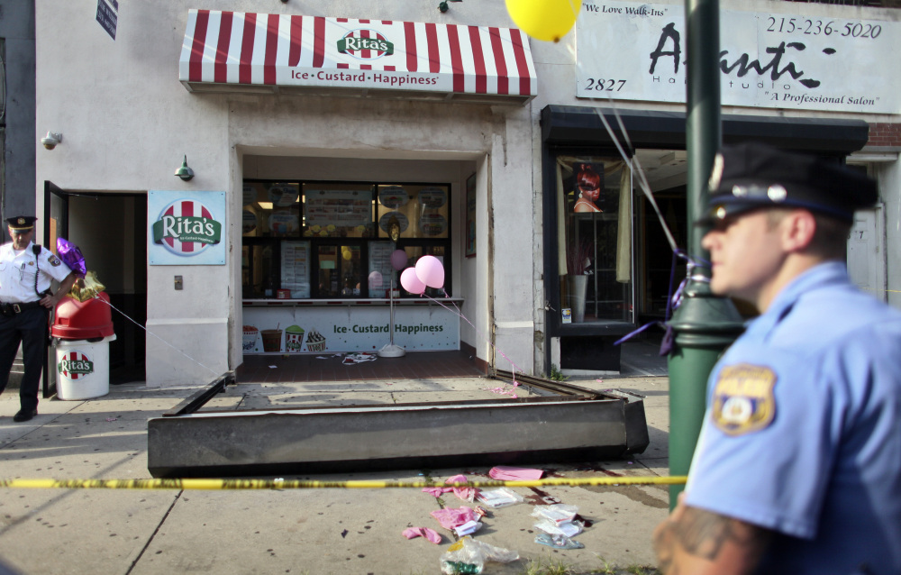 Investigators look over the debris of a fallen security door at a Rita’s Water Ice store in Philadelphia on Saturday. The metal security grate detached, killing a 3-year-old girl.
