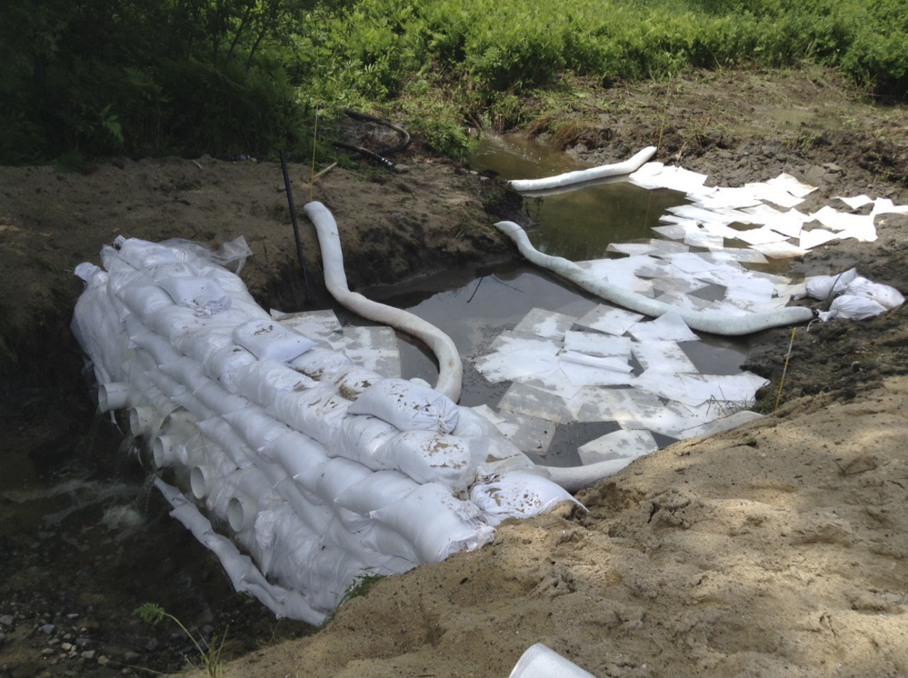 Underflow dams, reinforced with plastic bags filled with a solid substance to weigh down tubing and hold it in place, restrict the flow of oil in storm water systems on a naturally occurring wetland. The floating sheets are designed to soak up any oil on or just below the surface. These measures are part of the current phase of cleanup at the Gorham roundabout, where a tractor trailer spilled 9,000 gallons of fuel oil on June 11. Much of the oil has been vacuumed up or removed with conventional cleanup methods. 
 Source: Maine Department of Environmental Protection