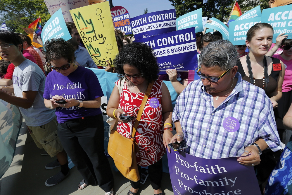 Demonstrators in support of abortion and contraceptive rights read on their mobile phones as the ruling for Hobby Lobby against their cause was announced outside the U.S. Supreme Court in Washington June 30, 2014. The U.S. Supreme Court on Monday ruled that business owners can object on religious grounds to a provision of U.S. President Barack Obama's healthcare law that requires closely held companies to provide health insurance that covers birth control. REUTERS/Jonathan Ernst (UNITED STATES - Tags: RELIGION POLITICS HEALTH CIVIL UNREST) - RTR3WGEF