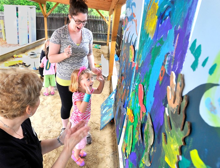 Evelyn Kirby, 3, expresses joy in her accomplishment of putting painted fish cutouts onto a painting of the ocean with speech-language pathologist Laurie Mack, left, of Northeast Hearing and Speech Center, and University of Southern Maine art education student Jacklyn Peters at Children's Odyssey, a pre-school in Portland on Thursday.