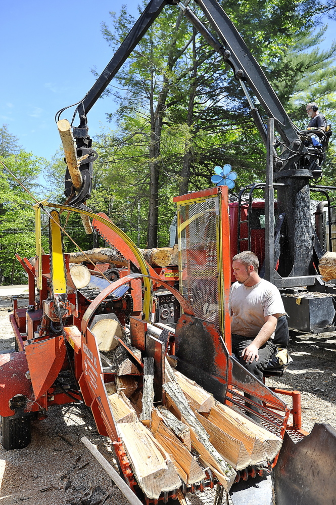 WINDHAM, ME - MAY 21: Mark Killinger, owner of Atlantic Firewood adds hardwood logs to the line as his son, Mike Killinger, owner of Maine Logging, tends the cutting and processing machine as they work together to cut and process firewood for sale. (Photo by Gordon Chibroski/Staff Photographer)
