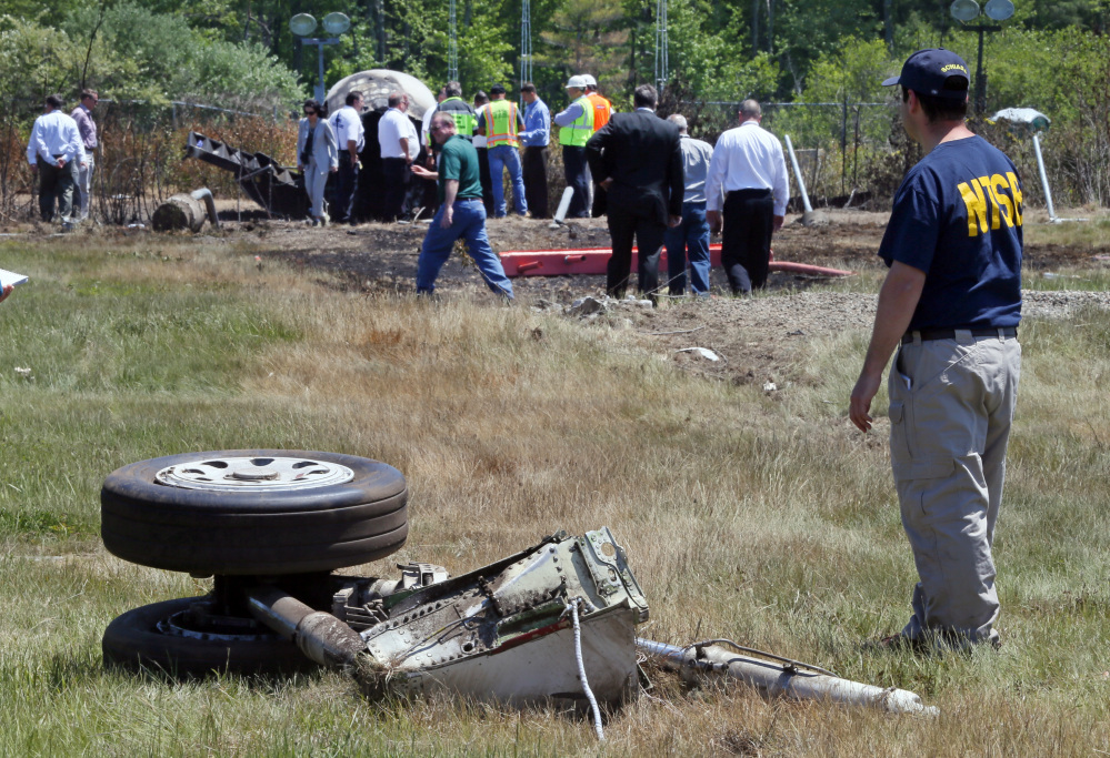 A National Transportation Safety Board official stands beside a piece of the landing gear at the scene Monday, June 2, 2014, in Bedford, Mass., where a plane plunged down an embankment and erupted in flames during a takeoff attempt at Hanscom Field on Saturday night. The Associated Press