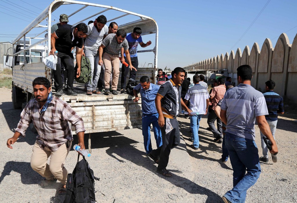 Iraqi men jump out of a truck at the main recruiting center as they volunteer for military service in Baghdad, Iraq, Tuesday, June 24, 2014, after authorities urged Iraqis to help battle insurgents.