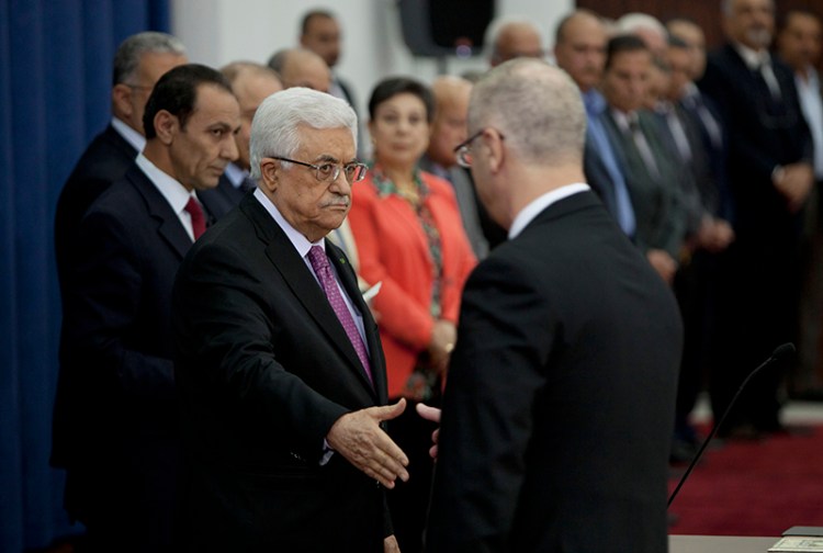 Palestinian Prime Minister Rami Hamdallah, right, extends his hand to shake hands with Palestinian President Mahmoud Abbas during a swearing-in ceremony of the unity government in the West Bank city of Ramallah on Monday. The Associated Press