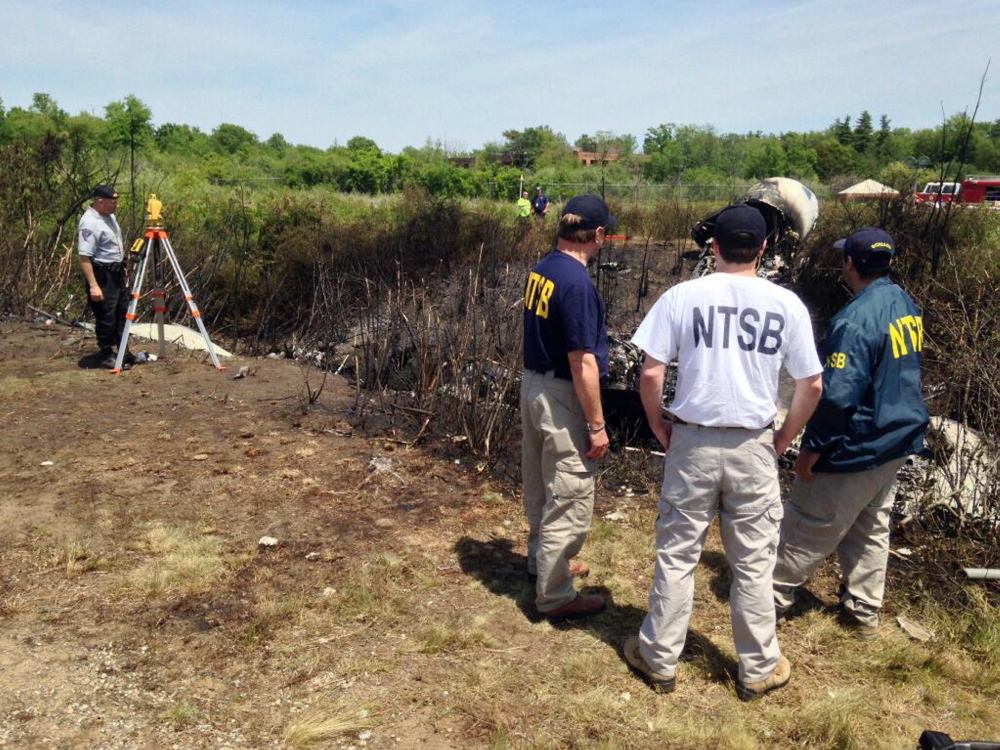 This photo provided by the National Transportation Safety Board, shows NTSB investigators at the scene of a plane that plunged down an embankment and erupted in flames during a takeoff attempt Saturday night at Hanscom Field in Bedford, Mass. The Associated Press
