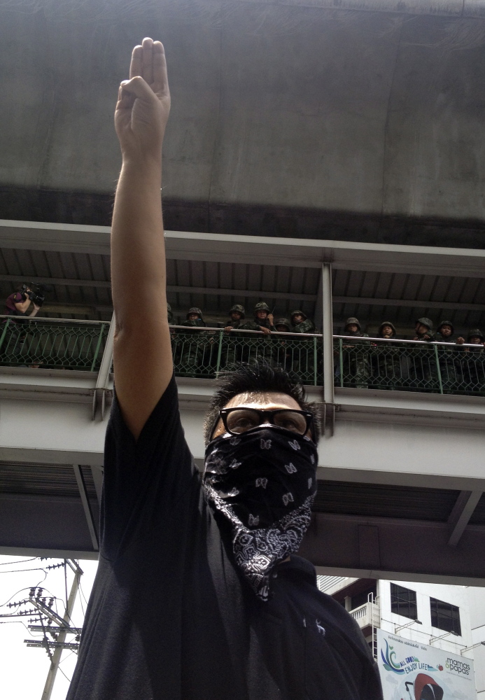 The Associated Press An anti-coup protester gives a three-finger salute as soldiers keep eyes on him from an elevated walkway near a rally site in central Bangkok on Sunday. Thailand’s military rulers say they are monitoring the new form of silent resistance to the coup.