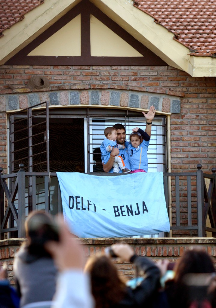 Uruguay's soccer player Luis Suarez, with his children Benjamin, left, and Delfina, waves to fans from his home, before the start of his team's World Cup round 16 match with Colombia, from which he was banned and Uruguay lost.