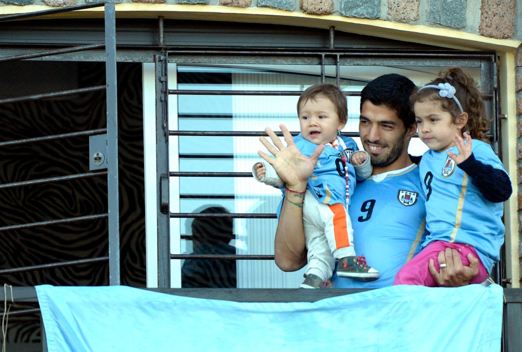 Uruguay's soccer player Luis Suarez, center, with his children Benjamin, left, and Delfina, waves to fans from his home, before the start of his team's World Cup round 16 match with Colombia, on the outskirts of Montevideo, Uruguay, Saturday, June 28, 2014. FIFA banned Suarez from all football activities for four months for biting an opponent at the World Cup.
